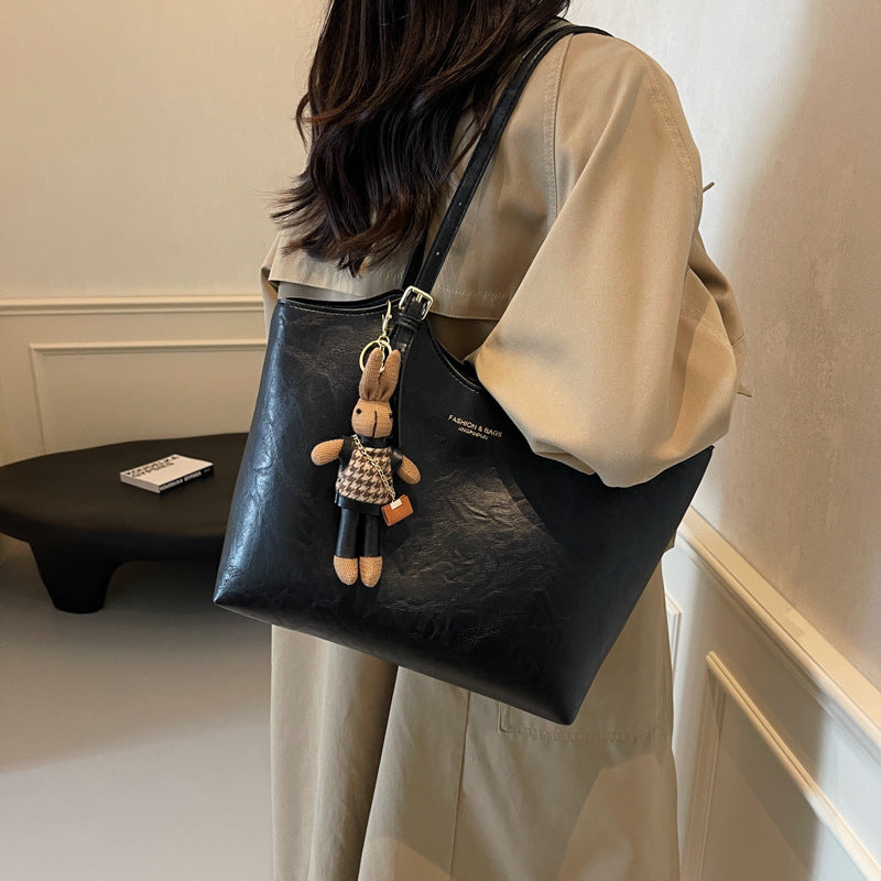 Person holding a black leather bag with a teddy bear keychain, wearing a beige outfit.
women’s leather tote, waxed leather bag, artisan leather handbag, everyday leather tote, casual leather bag, handcrafted leather tote, durable leather handbag, stylish leather tote, versatile leather carryall, spacious leather shoulder bag